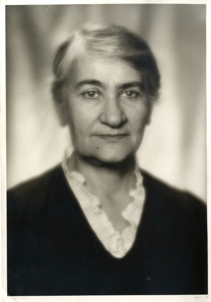Black and white photo of a white woman with greying hair dressed in black with a white collar.