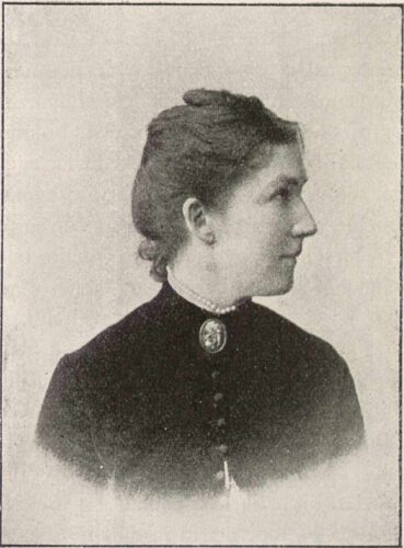 a black and white photograph of a white woman in a high neck black top with a broach.