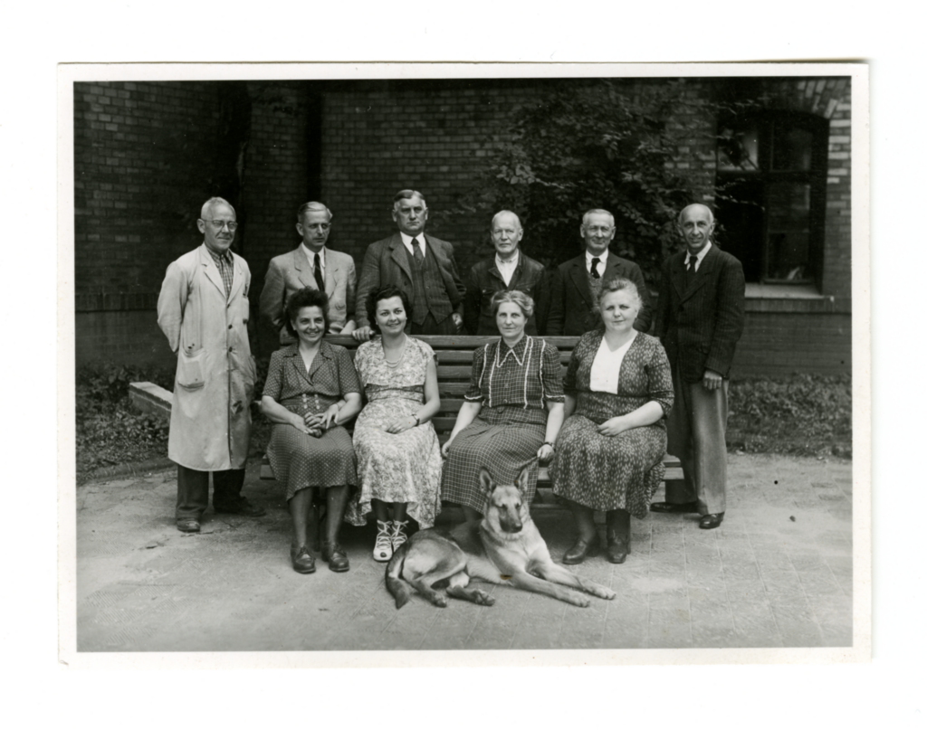 Group photo of 10 people, 4 women sitting, 6 men standing at the back with a dog lying down at the front.