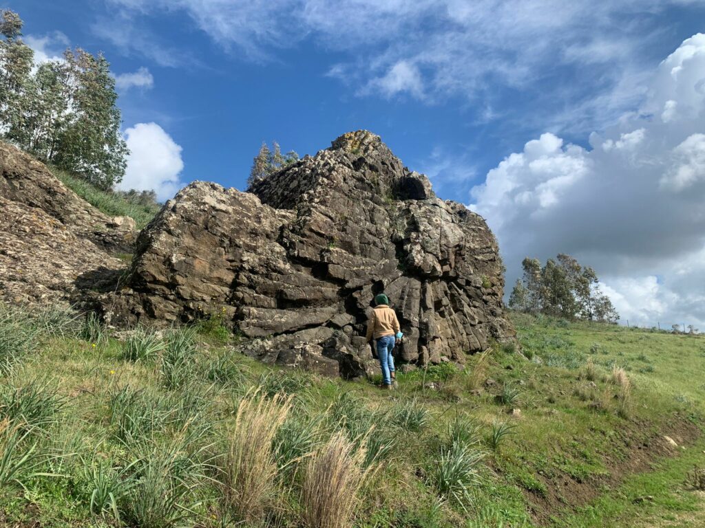 A colour photograph of a stone structure in a field with a person walking up to it.